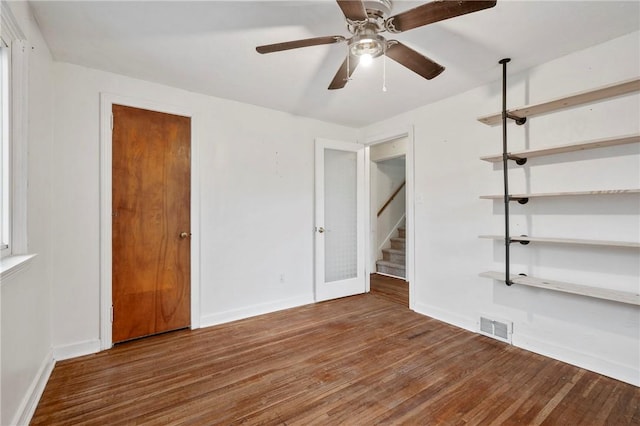 empty room with stairway, baseboards, visible vents, and dark wood-type flooring