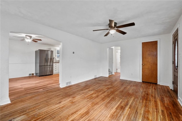 spare room featuring light wood-style floors, visible vents, arched walkways, and a ceiling fan