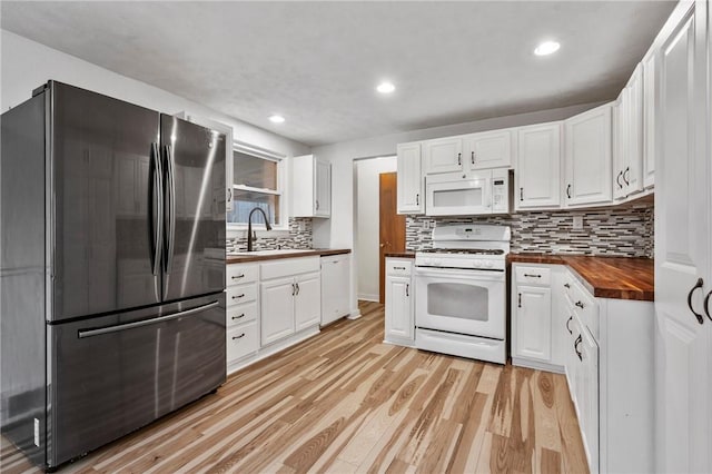 kitchen featuring butcher block counters, light wood-style flooring, white cabinetry, a sink, and white appliances