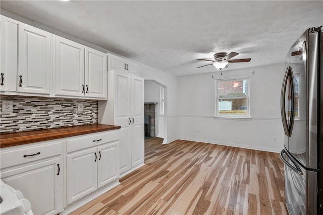 kitchen with butcher block counters, backsplash, freestanding refrigerator, white cabinets, and light wood-type flooring