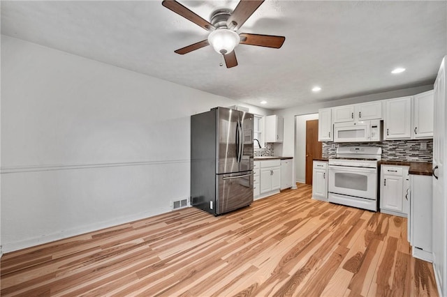 kitchen with white appliances, dark countertops, light wood-style flooring, and white cabinetry