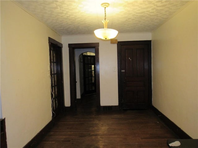 hall with a textured ceiling, baseboards, dark wood finished floors, and arched walkways