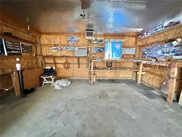 miscellaneous room featuring a garage, a workshop area, a wall mounted AC, and concrete flooring