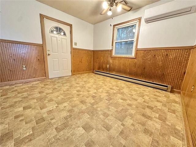 empty room with a wall mounted AC, a ceiling fan, wainscoting, wood walls, and baseboard heating