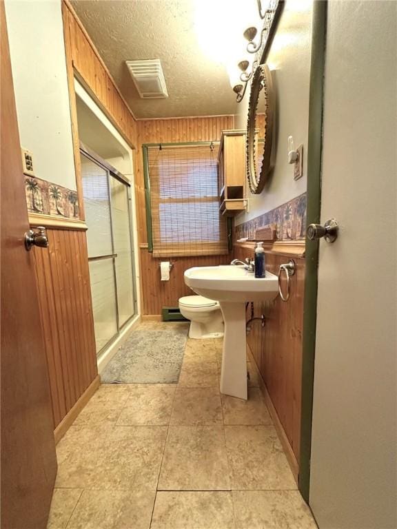 full bathroom featuring a textured ceiling, a shower stall, wood walls, baseboard heating, and toilet