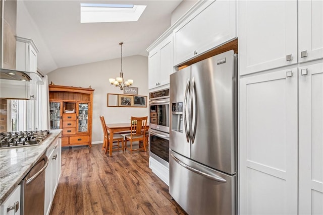 kitchen with white cabinets, lofted ceiling with skylight, appliances with stainless steel finishes, light stone counters, and hanging light fixtures