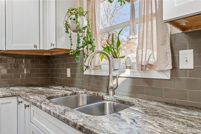 room details with light stone countertops, backsplash, white cabinets, and a sink