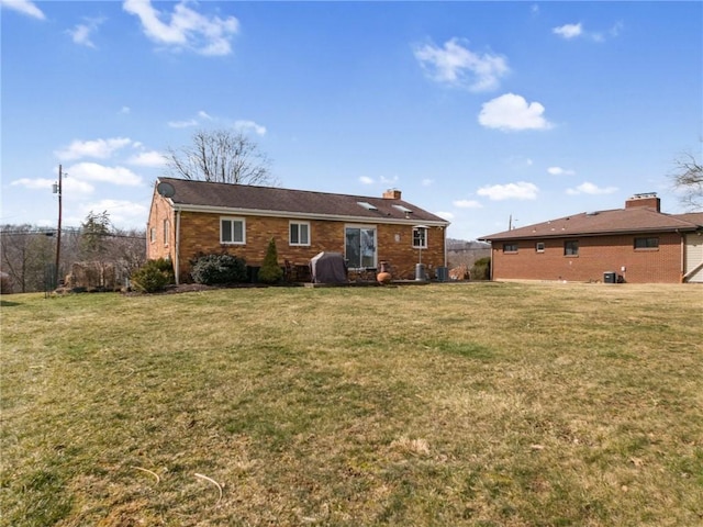 rear view of property featuring brick siding, a chimney, and a yard