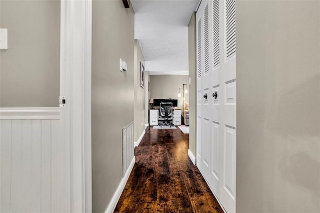 corridor featuring baseboards, visible vents, dark wood finished floors, and wainscoting