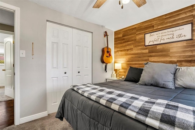 bedroom with carpet floors, a closet, an accent wall, a ceiling fan, and wood walls