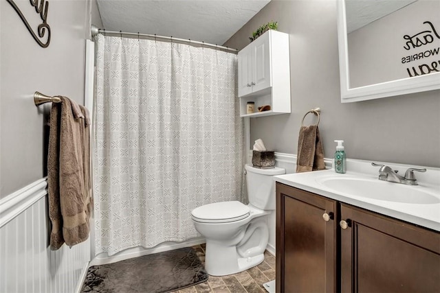 bathroom featuring toilet, a wainscoted wall, a textured ceiling, and vanity