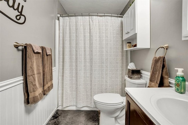 full bath with shower / tub combo with curtain, toilet, wainscoting, vanity, and a textured ceiling