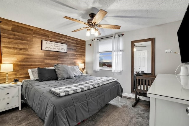 bedroom with a textured ceiling, an accent wall, dark carpet, and wooden walls