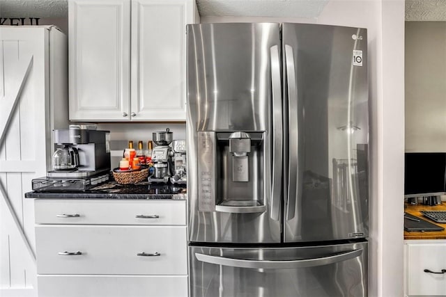 kitchen with a textured ceiling, stainless steel refrigerator with ice dispenser, white cabinetry, and dark stone countertops