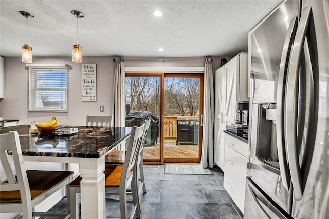 kitchen featuring plenty of natural light, hanging light fixtures, stainless steel refrigerator with ice dispenser, and white cabinets