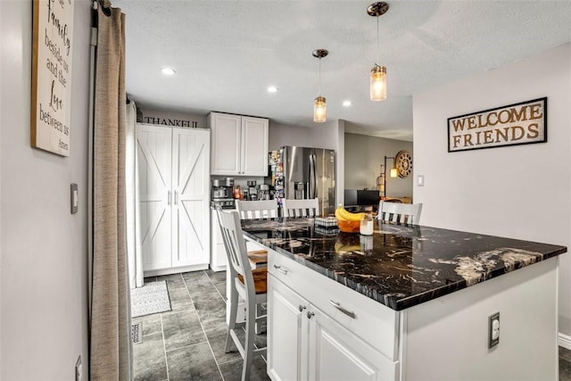 kitchen featuring a kitchen island, white cabinetry, stainless steel refrigerator with ice dispenser, dark stone counters, and pendant lighting