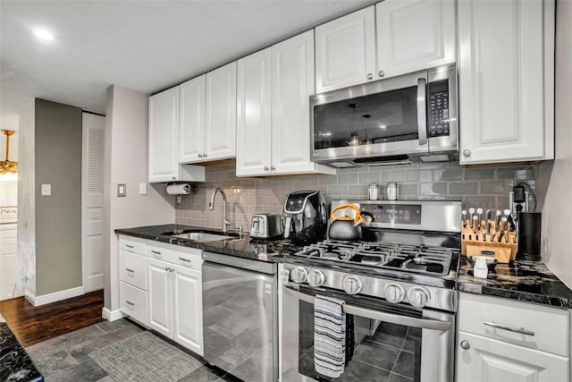 kitchen featuring tasteful backsplash, white cabinets, dark stone countertops, stainless steel appliances, and a sink