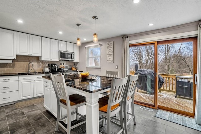 kitchen with a breakfast bar area, dark countertops, stainless steel microwave, hanging light fixtures, and a sink