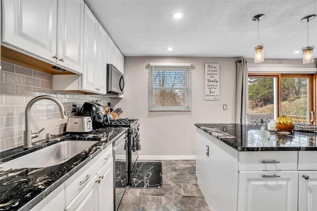 kitchen with decorative light fixtures, a sink, stainless steel appliances, white cabinetry, and a wealth of natural light