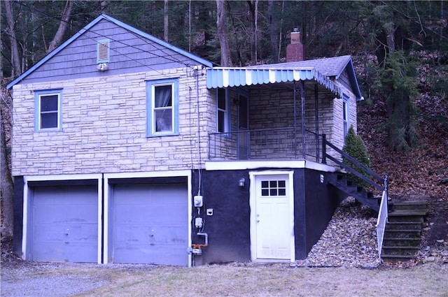 view of front of property with a garage, stairway, stucco siding, a forest view, and a chimney