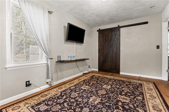 interior space with baseboards, a barn door, wood finished floors, and a healthy amount of sunlight