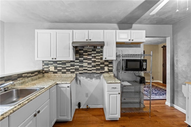 kitchen featuring black microwave, under cabinet range hood, dark wood-type flooring, a sink, and white cabinetry