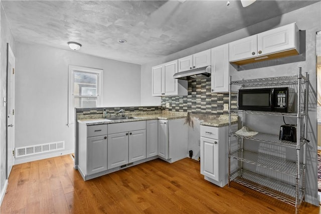 kitchen with visible vents, light wood-style floors, a sink, black microwave, and under cabinet range hood