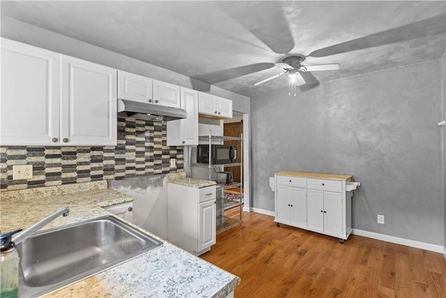 kitchen featuring under cabinet range hood, white cabinetry, black microwave, and a sink
