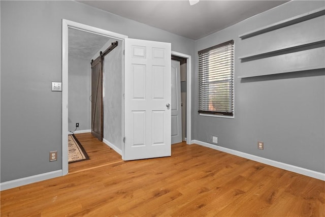 unfurnished bedroom featuring light wood finished floors, a barn door, and baseboards