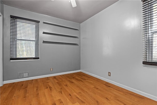 spare room with a ceiling fan, visible vents, baseboards, and wood finished floors