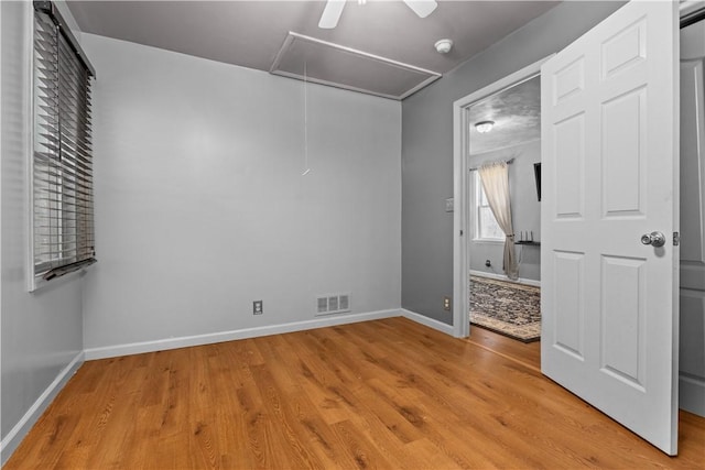 unfurnished bedroom with visible vents, light wood finished floors, attic access, and baseboards