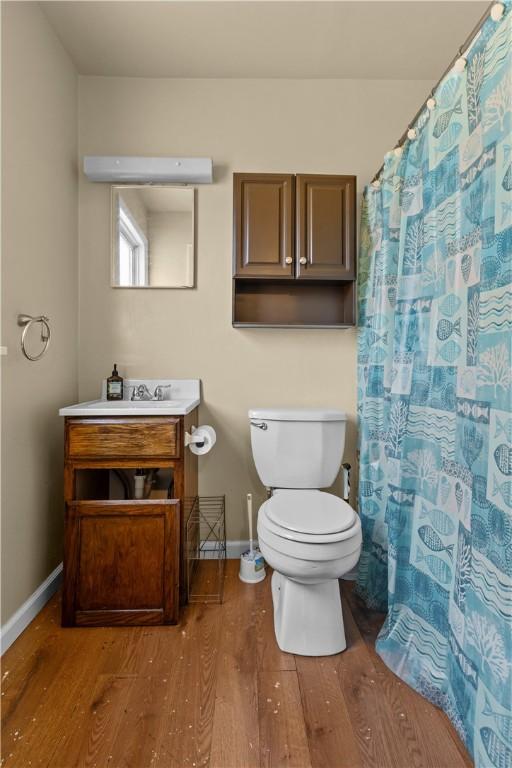bathroom with a shower with shower curtain, toilet, vanity, wood finished floors, and baseboards