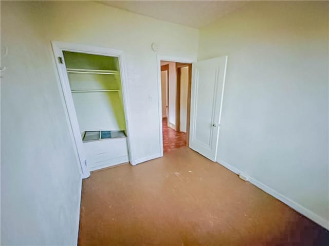 unfurnished bedroom featuring concrete floors, baseboards, and a closet