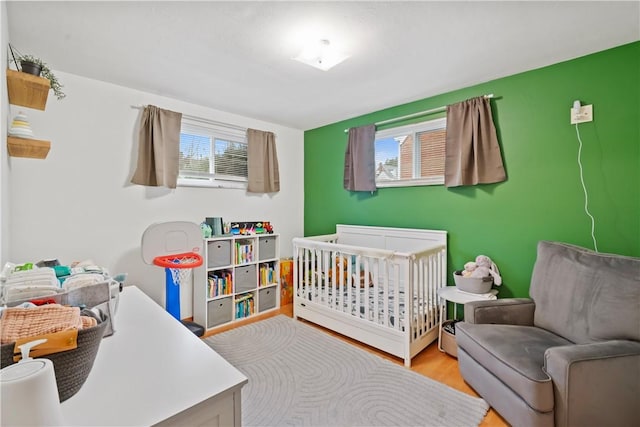 bedroom with a nursery area, multiple windows, and wood finished floors