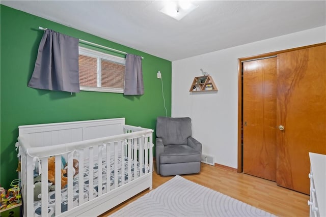 bedroom featuring a nursery area, wood finished floors, visible vents, and baseboards