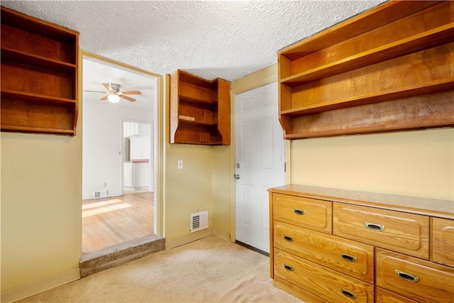 interior space featuring a textured ceiling, baseboards, visible vents, and light colored carpet