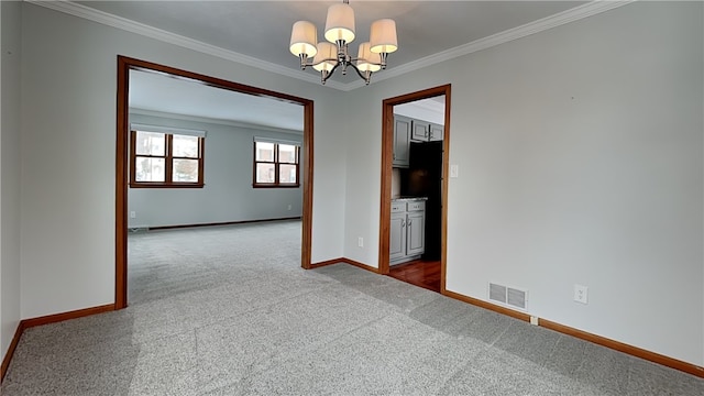 spare room featuring carpet, a notable chandelier, visible vents, ornamental molding, and baseboards