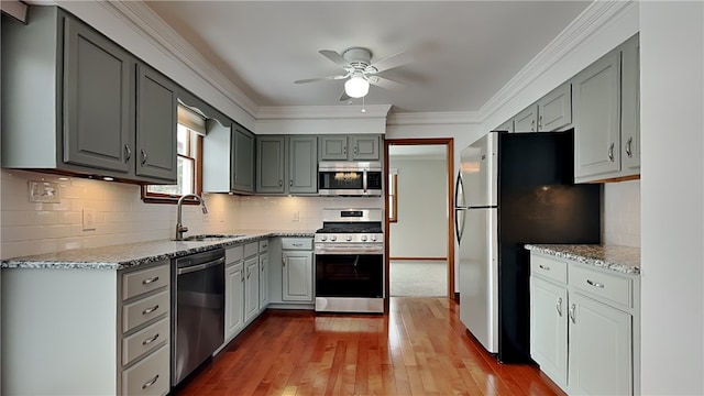 kitchen with appliances with stainless steel finishes, light stone counters, crown molding, gray cabinetry, and a sink