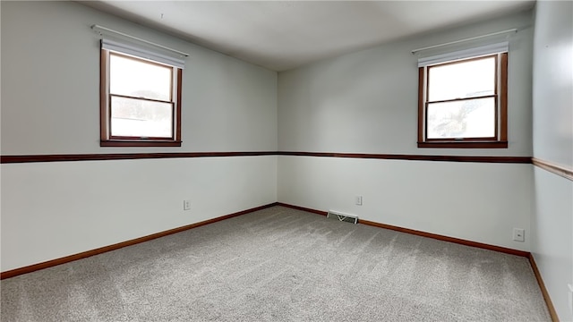 unfurnished room featuring a wealth of natural light, carpet flooring, visible vents, and baseboards