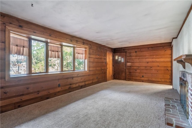 unfurnished living room featuring a glass covered fireplace, carpet flooring, and wooden walls