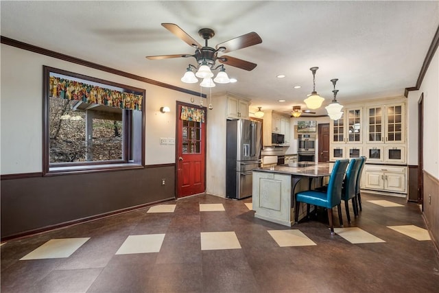 kitchen featuring wainscoting, cream cabinets, a breakfast bar, and stainless steel fridge with ice dispenser