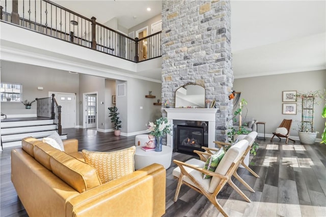 living room with a stone fireplace, wood finished floors, a towering ceiling, baseboards, and stairway