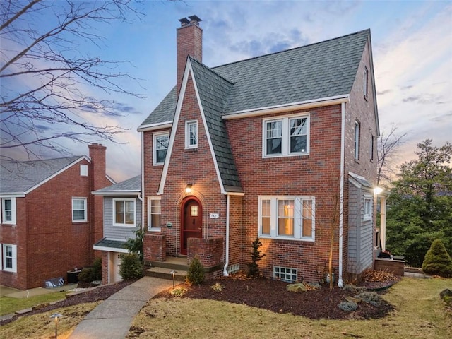 tudor house featuring brick siding, a chimney, and roof with shingles