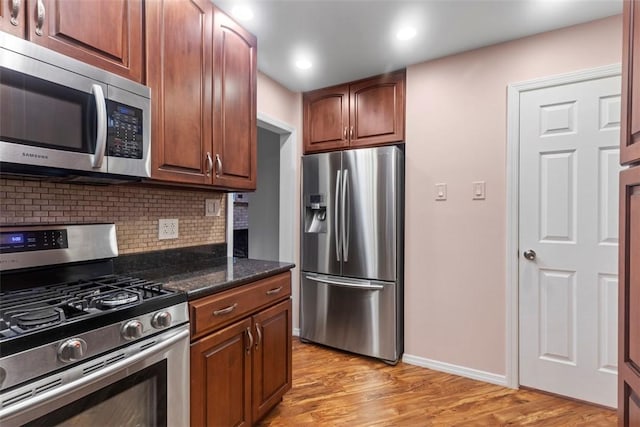 kitchen with light wood-type flooring, baseboards, appliances with stainless steel finishes, and decorative backsplash