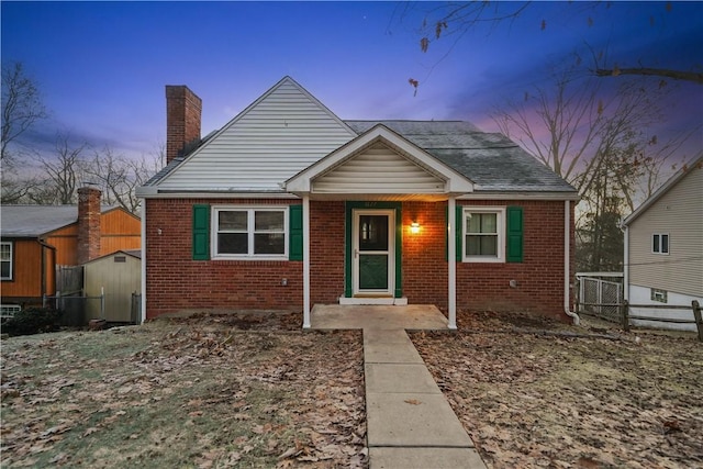 bungalow-style house with a chimney, fence, and brick siding