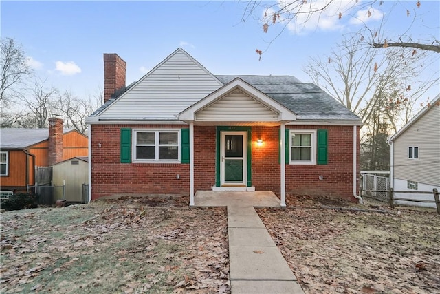 bungalow-style house featuring brick siding, fence, and a chimney