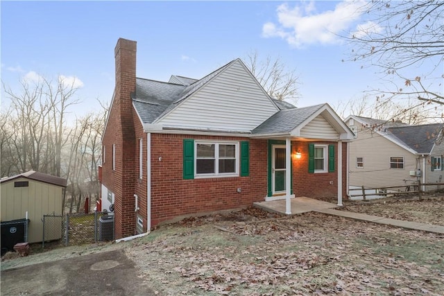 bungalow-style home featuring a shingled roof, a chimney, fence, an outdoor structure, and brick siding