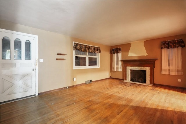 unfurnished living room featuring wood finished floors, a fireplace with flush hearth, visible vents, and baseboards