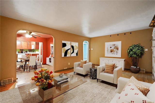 living area featuring arched walkways, visible vents, a ceiling fan, light wood-type flooring, and baseboards