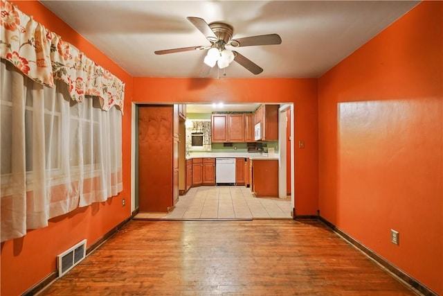 kitchen with white appliances, light wood finished floors, visible vents, brown cabinetry, and light countertops